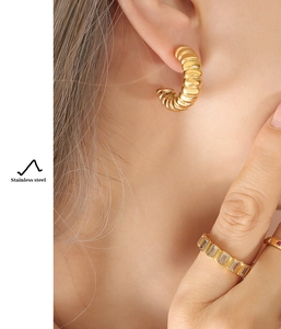 Detailed shot of gold C-shaped twisted rope earrings and zircon ring in stainless steel