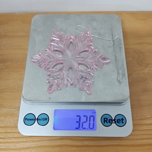 Macro detail of a 32g pink acrylic snowflake pendant on a digital scale for weight check