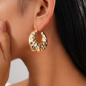 Gros plan de boucles d'oreilles dorées martelées sur un mannequin avec texture métallique