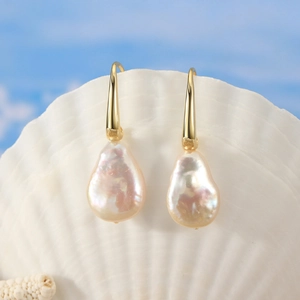 Baroque pearl drop earrings with gold hooks displayed on a shell with sea background