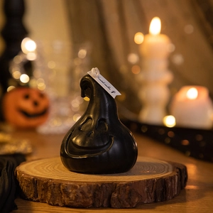Detail of a black ghost pumpkin scented candle on a rustic wood slice for Halloween decor