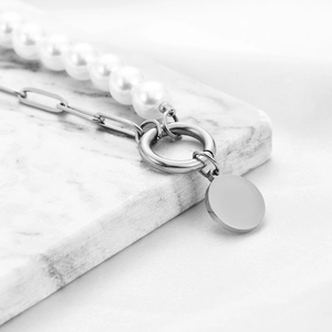 Close-up of pearl and paperclip chain necklace with a polished round pendant on marble