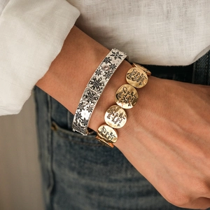 Ensemble bracelet manchette flocon gravé et perles dorées porté au poignet d'une femme