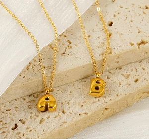 Detail view of golden balloon style letter A and B pendants on a satin background