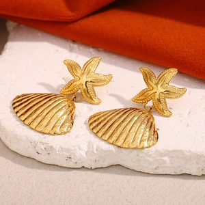 Gold-plated stainless steel starfish shell earrings on a white stone textured pedestal