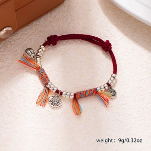 Detail of red braided bracelet with silver fortune pendants and colorful tassels
