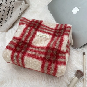 Gedetailleerde textuur van rode geruite pluche make-up tas op wit tapijt met decor