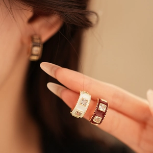 Detail of C-shaped gold-plated earrings with colorful enamel and zircon stones