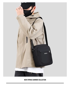 Man wearing a black waterproof nylon crossbody bag against a minimalist grey background