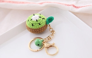 Macro detail of handmade crochet kiwi keychain with green yarn and golden bell clip