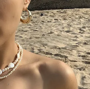 Nahaufnahme goldener Creolen und einer zweilagigen Barockperlenkette an einem Modell