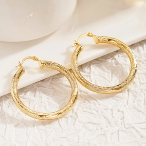 Dettaglio di orecchini a cerchio placcati oro con texture effetto corteccia e chiusura