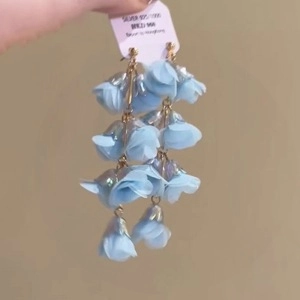 Détail de boucles d'oreilles fleurs en tissu bleu clair avec pétales et clous en argent 925