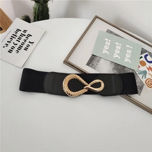 Elastic black waist belt with interlocking gold oval buckle on a minimalist white surface