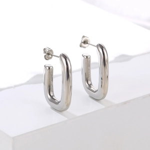Minimalist silver U-shaped stainless steel earrings on a clean white geometric base