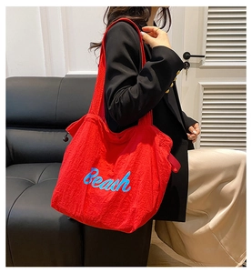 Detail of red nylon tote bag with blue Beach lettering worn by a model in casual style