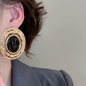 Dettaglio di orecchini vintage dorati martellati con una grande gemma ovale nera sul modello