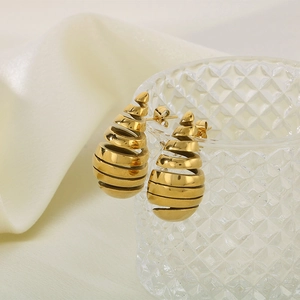 Detail of gold spiral teardrop earrings hanging on textured glass with silk background