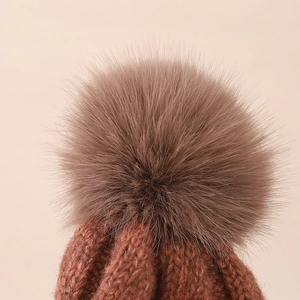Detail of winter knit hat featuring a fluffy faux fur pom-pom and thick ribbed texture