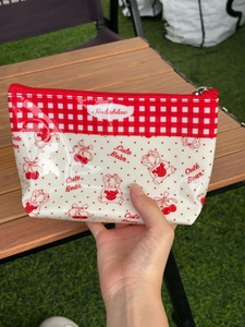Red cherry and bear print waterproof PVC storage pouch held against a garden background