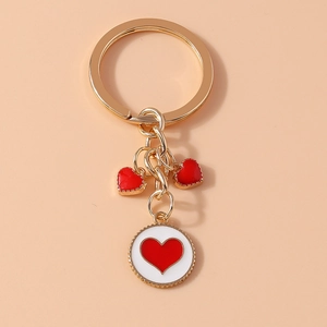 Detail of a gold metal keychain featuring red enamel hearts and a round logo charm