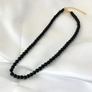 Detail shot of black onyx bead necklace with gold lobster clasp on white silk fabric