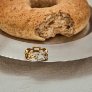 Anello a catena dorato con zirconi bianchi su un vassoio in metallo spazzolato
