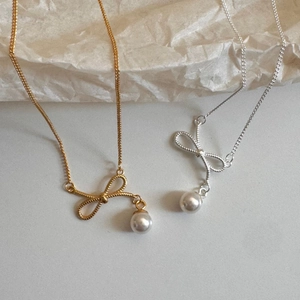 Detailed close-up of bow knot pearl pendants in gold and silver with woven texture