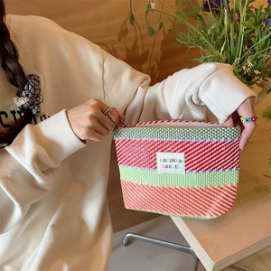 Detail of hand opening a colorful striped woven makeup bag with a zipper closure