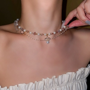 Detail of a double-layered necklace with pearls, pink crystals, and a zircon crown pendant