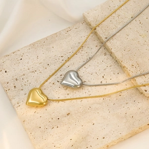 Close-up of 18k gold and silver puffy heart pendants on sleek snake bone chains