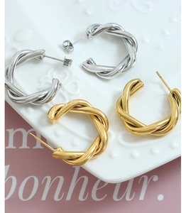 Close-up of C-shaped twisted earrings in gold and silver finish on a textured plate
