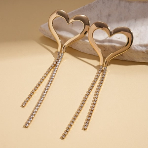 Macro view of gold heart earrings with dangling zircon tassels on a textured stone
