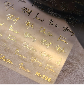 Macro detail of M-396 gold embossed nail stickers with stylish cursive typography
