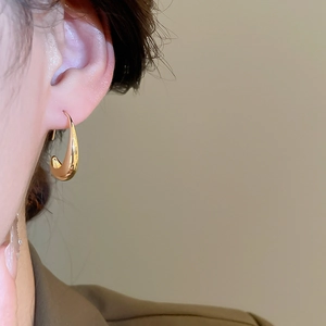 Close-up of 14k gold plated geometric oval hoop earring worn on ear for a luxury look