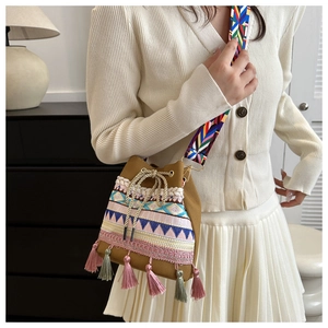 Ethnic style bucket bag with colorful tassels and woven strap shown on a model