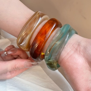 Detail of wide resin bracelets with marble texture in amber, caramel and dark green