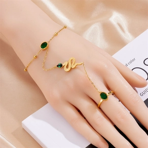 Detail of gold snake hand chain with emerald stones draped over soft pink silk fabric