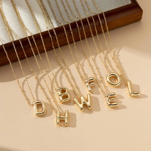 Detailed view of 3D bubble initial necklaces in gold finish on a wooden jewelry display