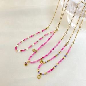Detail of beaded gold necklaces with pink stones, pearls and floral charms on silk