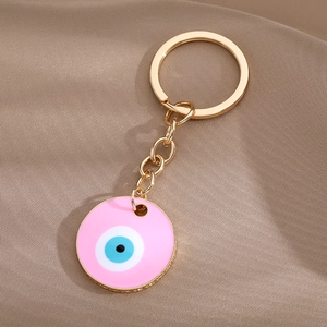 Close-up of pink enamel evil eye keychain with gold alloy finish on textured fabric