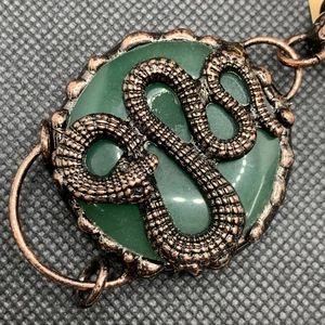Macro detail of a bronze snake motif coiled on a green crystal stone pendant