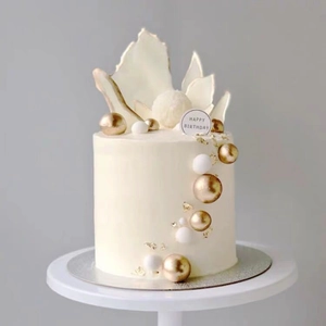 Detail of elegant white cake with gold and white sphere toppers and leaf decorations