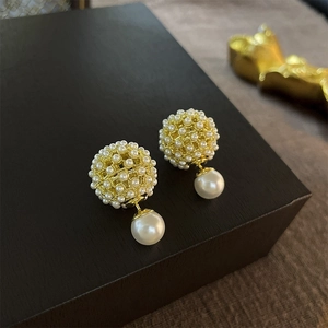 Close-up of gold plated cluster earrings with white pearls on a black jewelry box
