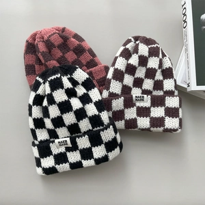 Close-up of three checkered knit beanies in black, brown, and pink with labels.