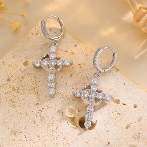 Macro view of silver cross earrings with clear zircon stones on a textured stone surface