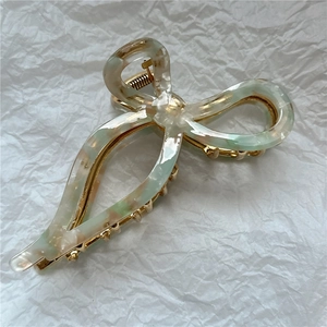 Macro detail of acetate bow hair claw clip showing marble green texture and golden spring