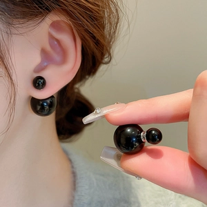Detail of dual-pearl black earrings showing glossy finish and ear placement