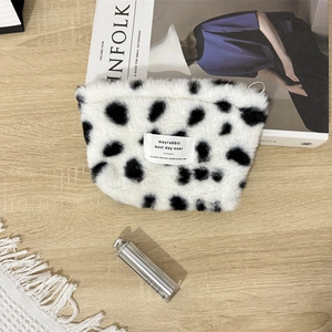 Macro detail of plush cow print makeup bag with woven label on wooden background