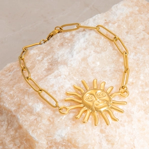 Close-up of a gold stainless steel bracelet featuring a retro sun face pendant on a rock